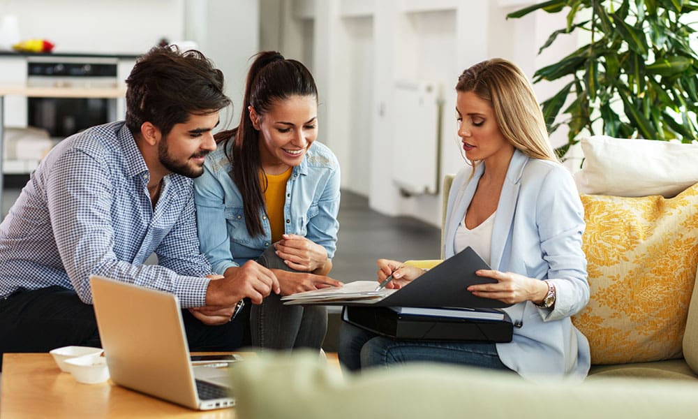 Blog - Woman Showing Couple Notes and Documents in their Living Room While Sitting on the Couch in Front of a Laptop