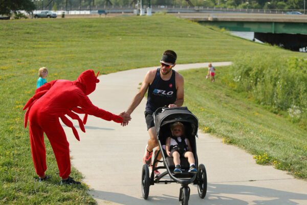 Photo of man running with stroller high-fiving someone in a crawfish costume