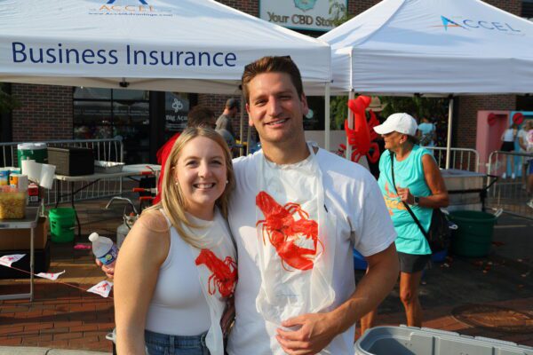 Man and woman smiling in front of The Accel Group tents in eating bibs with crawfish