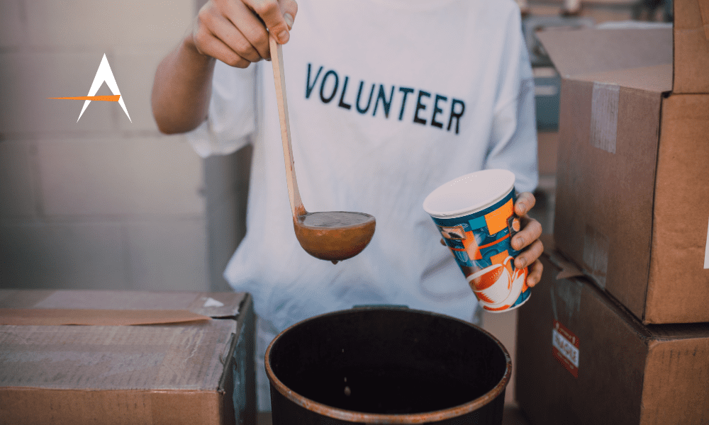 An image of a person wearing a 'volunteer' shirt serving soup outdoors